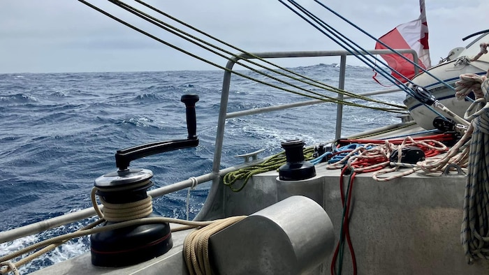 Un gros plan sur de l'équipement et du cordage à bord d'un voilier, d'où on voit la mer agitée et des vagues à l'horizon.
