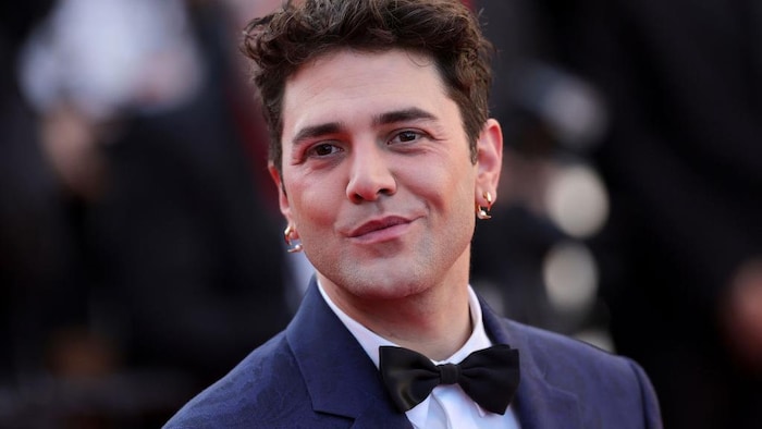 Xavier Dolan sourit sur un tapis rouge.