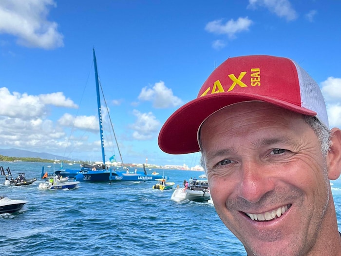 Danny Nadeau souriant devant une baie où des voiliers voguent.