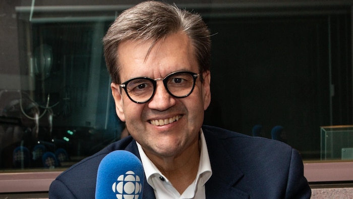 L'ex-maire de Montréal sourit à la caméra devant un micro dans un studio de radio.
