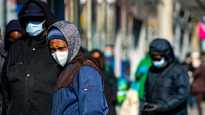 Des personnes portant un masque attendent en file sur un trottoir.