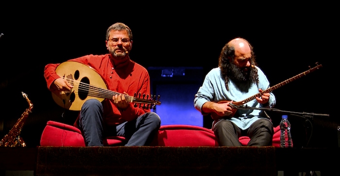 Charbel Rouhana et Kiya Tabassian joue du sétar et du oud. Ils sont assis sur un coussin rouge.