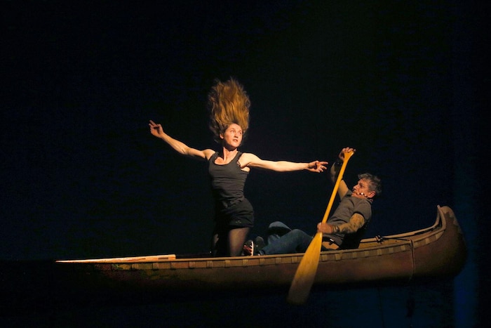 Dans un canot, une femme est à genoux et a les cheveux dressés sur la tête, tandis qu'un homme rame.