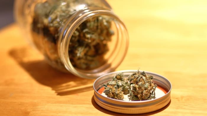 Un pot Masson renversé sur le côté avec de la marijuana à l'intérieur ainsi que dans le couvercle du pot, qui est ouvert et déposé sur une table.