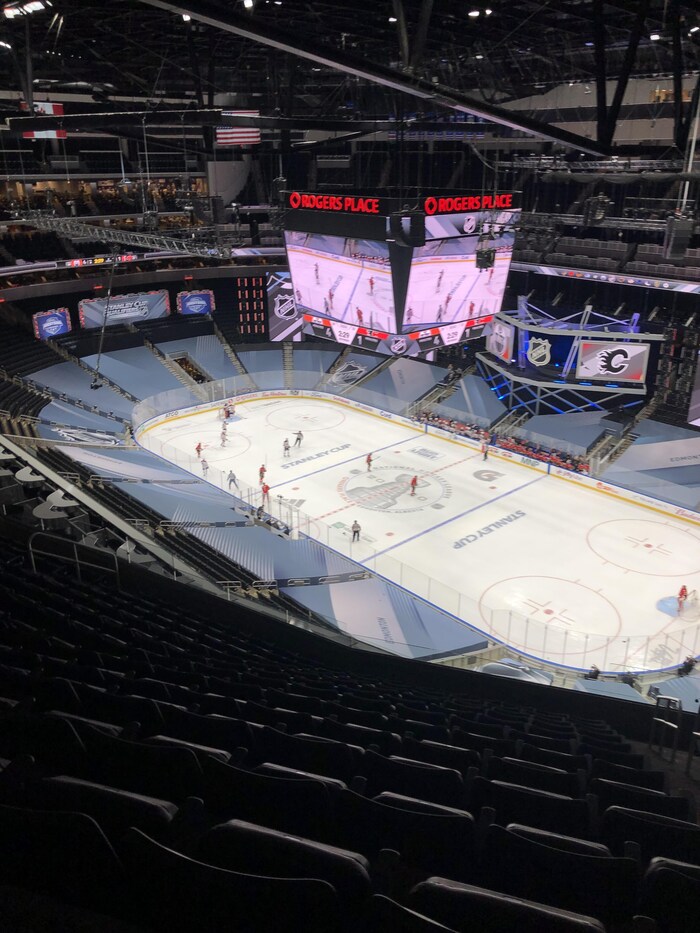 Des joueurs de hockey qui pratique sur la glace, sont diffusé en simultané sur l'écran géant de la place Rogers, avec les sièges vides.
