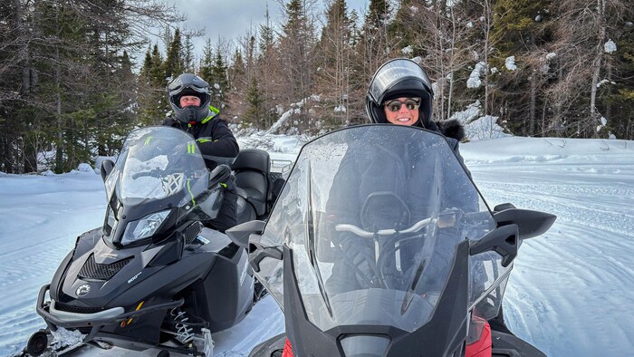 Deux motoneigistes sur leurs véhicules en hiver.