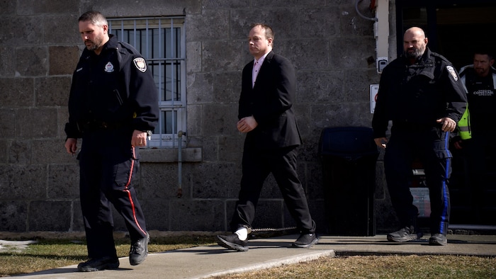 Alain Bellefeuille sort du palais de justice, menottes aux chevilles.