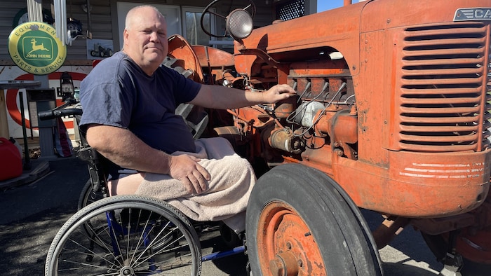Un homme en fauteuil roulant qui répare un tracteur orange.