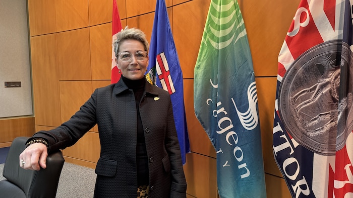 Alanna Hnatiw pose dans la chambre du conseil du comté de Sturgeon devant des drapeaux de l'Alberta, du Canada et du comté. 