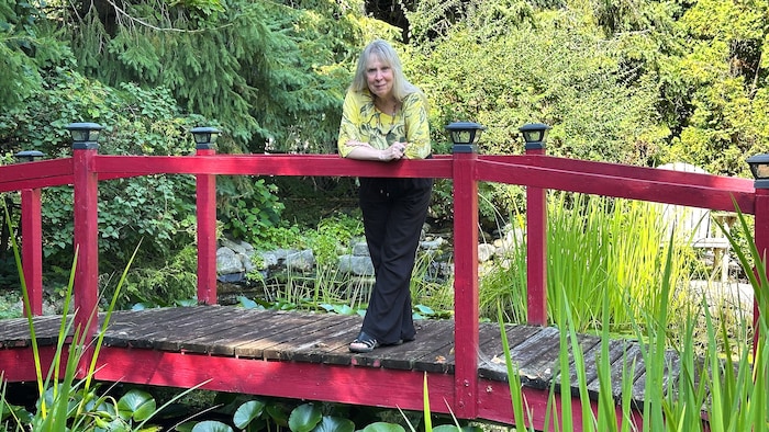Une femme qui pose sur un pont au-dessus d'un &eacute;tang. Elle est appuy&eacute;e sur le pont.