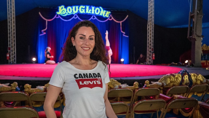 Anouchka Bouglione sourit debout devant la scène où des artistes sont en répétition.