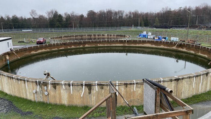 Un bassin de rétention d'eau qui ressemble à une immense piscine hors terre avec de l'eau verte dedans.