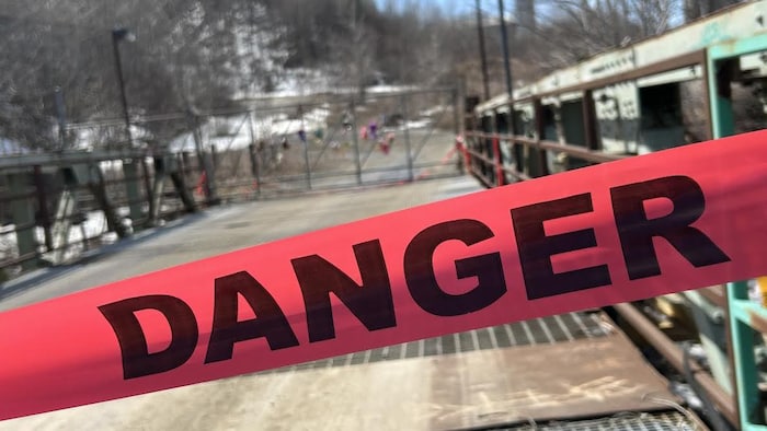 Un bandeau danger bloque une entrée d'un site industriel désaffecté.