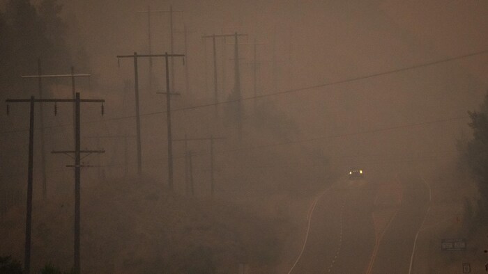 Un véhicule conduit à travers la fumée épaisse sur l'autoroute 97 entre Penticton et Summerland près du feu Bald Range à Summerland, Colombie-Britannique, le samedi 8 août 2026.