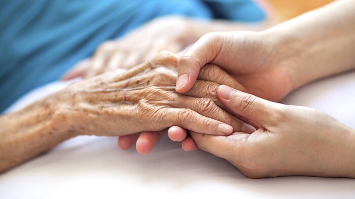 Deux mains de jeune femme tiennent la main d'une personne âgée.