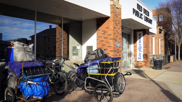 L'extérieur de la bibliothèque à Red Deer en Alberta. Des vélos avec des boîtes et des sacs sont stationnés à côté des portes d'entrée.
