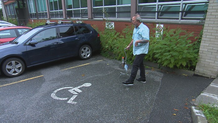 Dany marche avec une canne sur un stationnement. 
