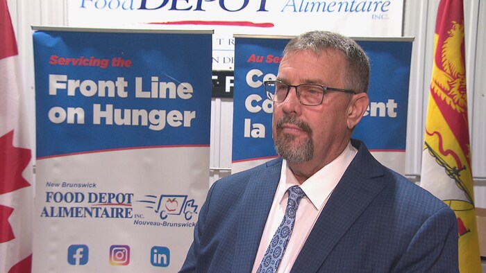 Bill Hogan debout devant des affiches et le drapeau du Nouveau-Brunswick.