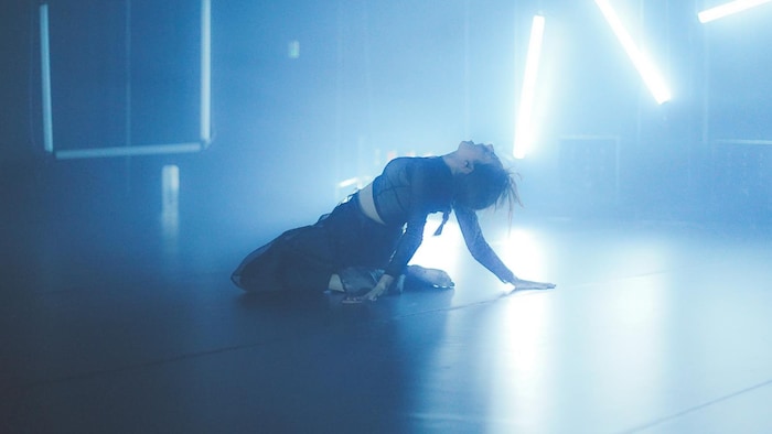 Une femme danse sur une scène. Plusieurs lumières bleues sont suspendues derrière elle.