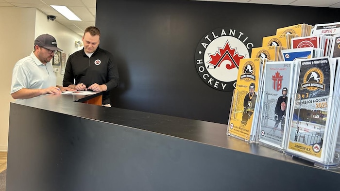 Two men behind the counter at Atlantic Hockey Group canadians sulk united states, tourist