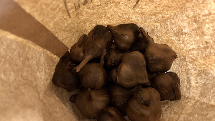 Des bulbes d'ail noir dans un sac en papier brun. 