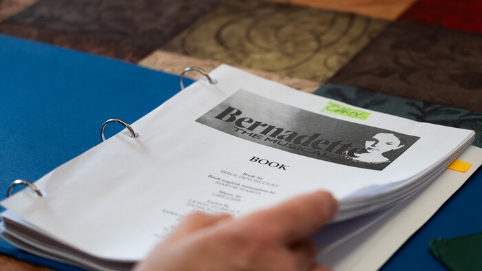 Une main feuillette un cartable de la production Bernadette The Musical.