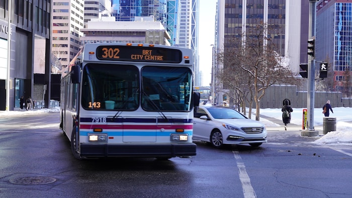 Autobus tournant dans une rue avec l'inscription du numéro de route ( 302 brt city centre ). Neige au sol, arbres sans feuille. Mars 2023.