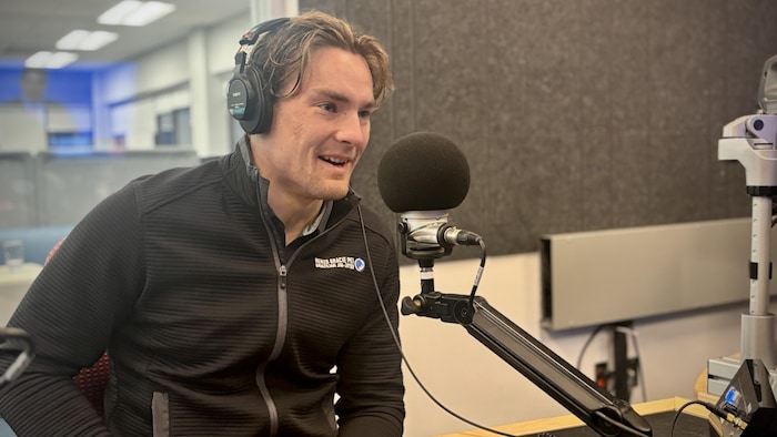 Cameron Nelson assit dans un studio radio derrière un micro.
