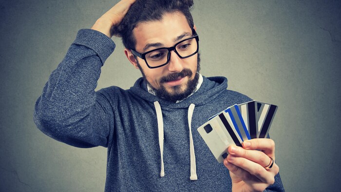 Un homme qui semble désespéré tient plusieurs cartes de crédit dans sa main.