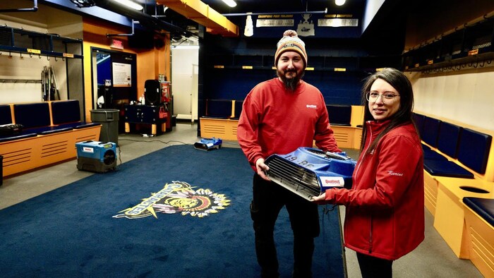 Deux personnes tiennent un ventilateur dans un vestiaire.