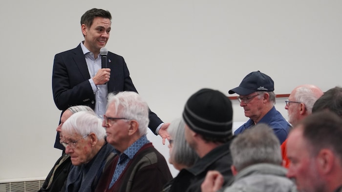Charles Milliard s'adresse à des gens assis dans une salle avec un micro dans les mains.