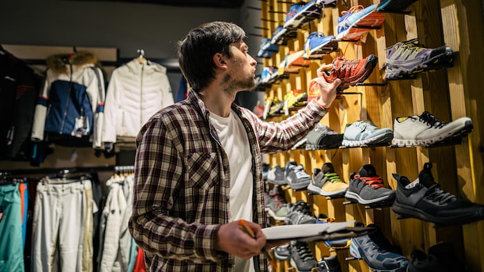 Un homme qui inspecte une chaussure qui est sur un mur d'un magasin de chaussures.