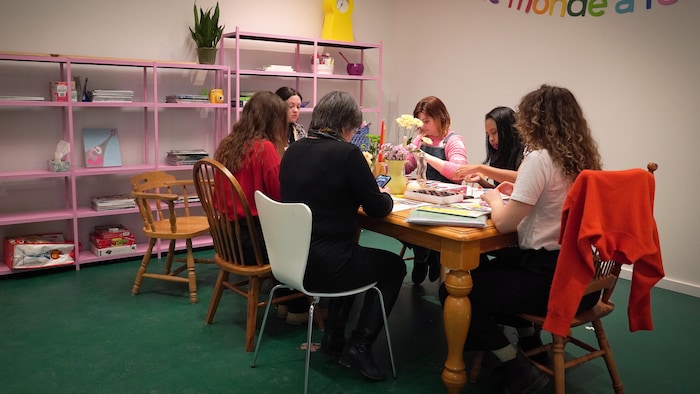 Plusieurs femmes assises autour d'une table. Elles font du bricolage.