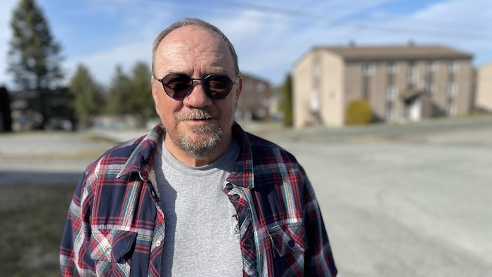 Un homme avec des lunettes de soleil regarde la caméra. 