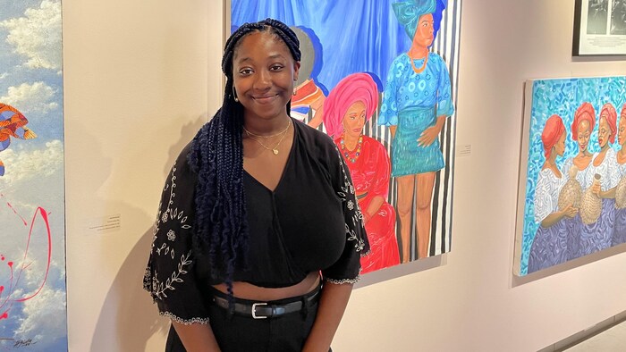 Delilah Edouard Williams, souriante, devant des oeuvres de l'exposition « Comme je t’aime », présentées sur un mur.