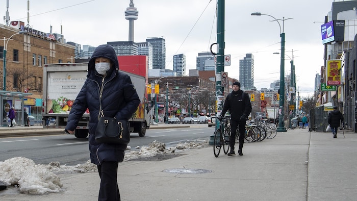 Une femme portant un masque sanitaire marche dans une rue du quartier chinois de Toronto.