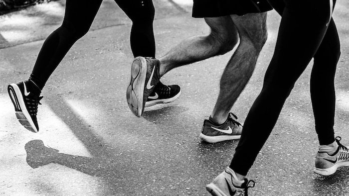Photo en noir et blanc des jambes et des pieds de trois personnes qui courent côte à côte.
