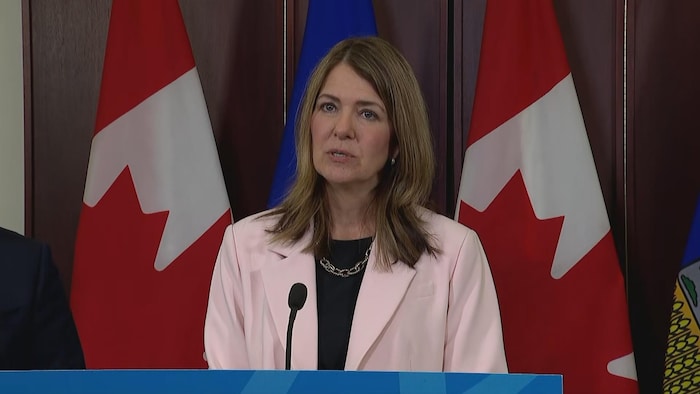 Danielle Smith parle au lutrin devant des drapeaux du Canada et de l'Alberta.