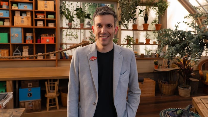 Un homme souriant qui pose dans un décor rempli de plantes.