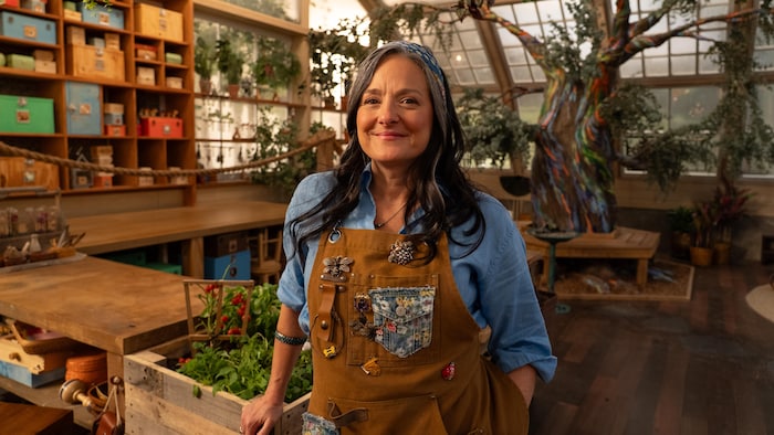Une femme souriante qui pose dans un décor rempli de plantes.