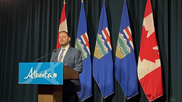 Le ministre parle devant un podium marqué Alberta devant une série de drapeaux albertains et canadiens. À Calgary le 30 juin 2025.