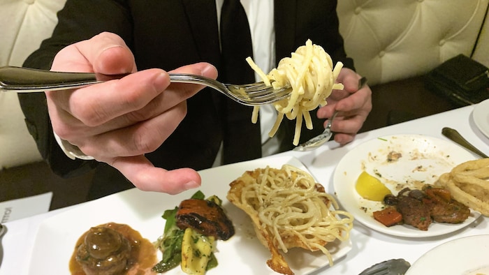 Gros plan d'une main qui tient une fourchette sur laquelle sont entourés des spaghettis.