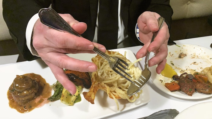 Gros plan d'une main qui tient une fourchette sur laquelle sont entourés des spaghettis.