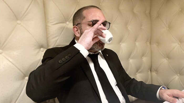 Un homme assis à une table d'un restaurant qui déguste un café avec le petit doigt levé.