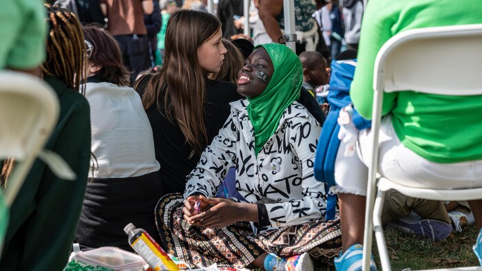 Une jeune fille portant un voile vert et un tatouage du drapeau franco-ontarien est assise dans l'herbe durant les célébrations.