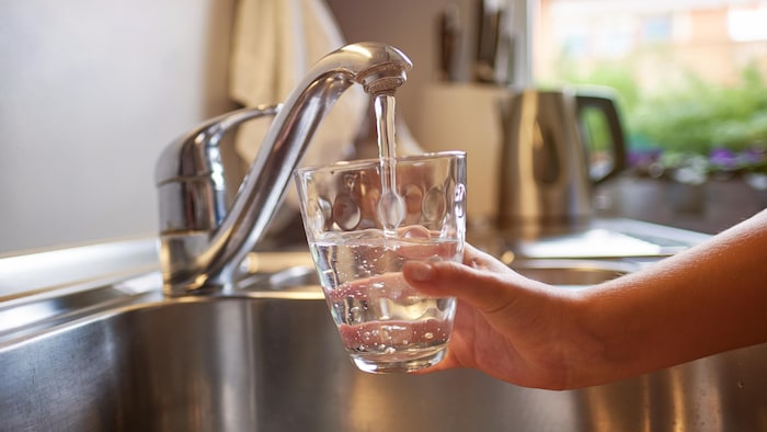 Gros plan d'une personne qui remplit un verre d'eau grâce au robinet d'un évier.