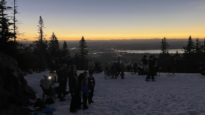 Des gens observent l'éclipse sur une montagne enneigée. 