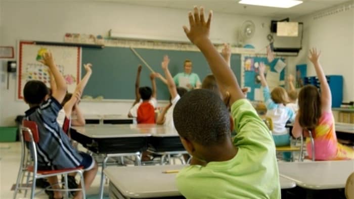 Des enfants assis sur leur chaise dans la classe lèvent la main.