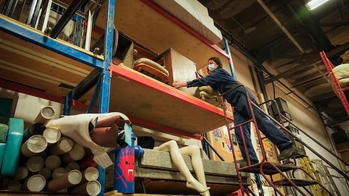 Une femme sur une échelle qui tient un meuble en bois sur une étagère dans un grand entrepôt.