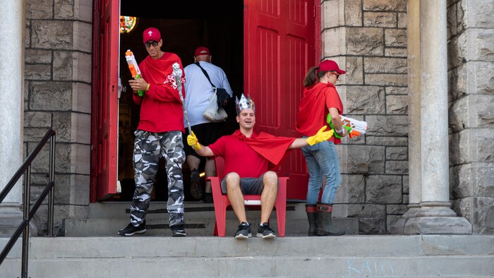 Des personnes vêtues de chandails rouges et munies de fusils à eau sur le parvis d'une église